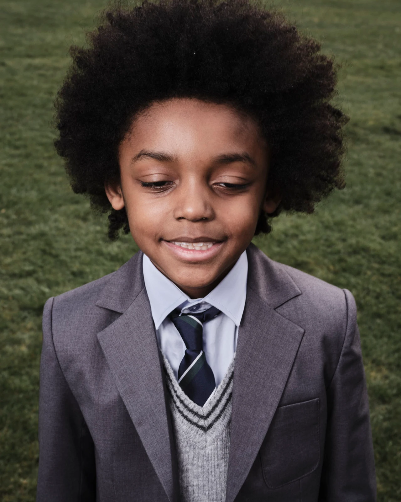A student in a grey blazer and striped tie relaxing on the grass